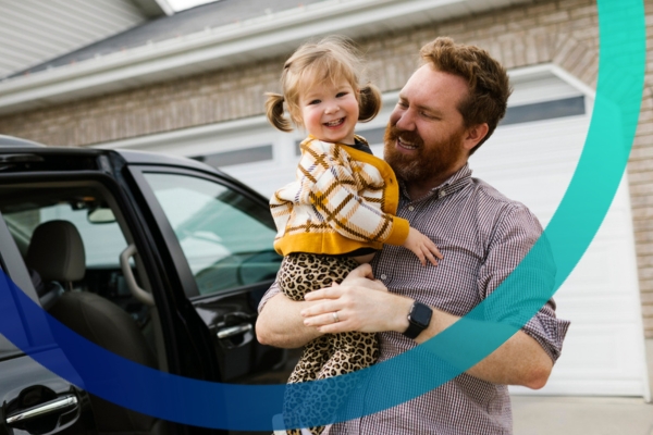 Dad holding daughter in drive way by van smiling.
